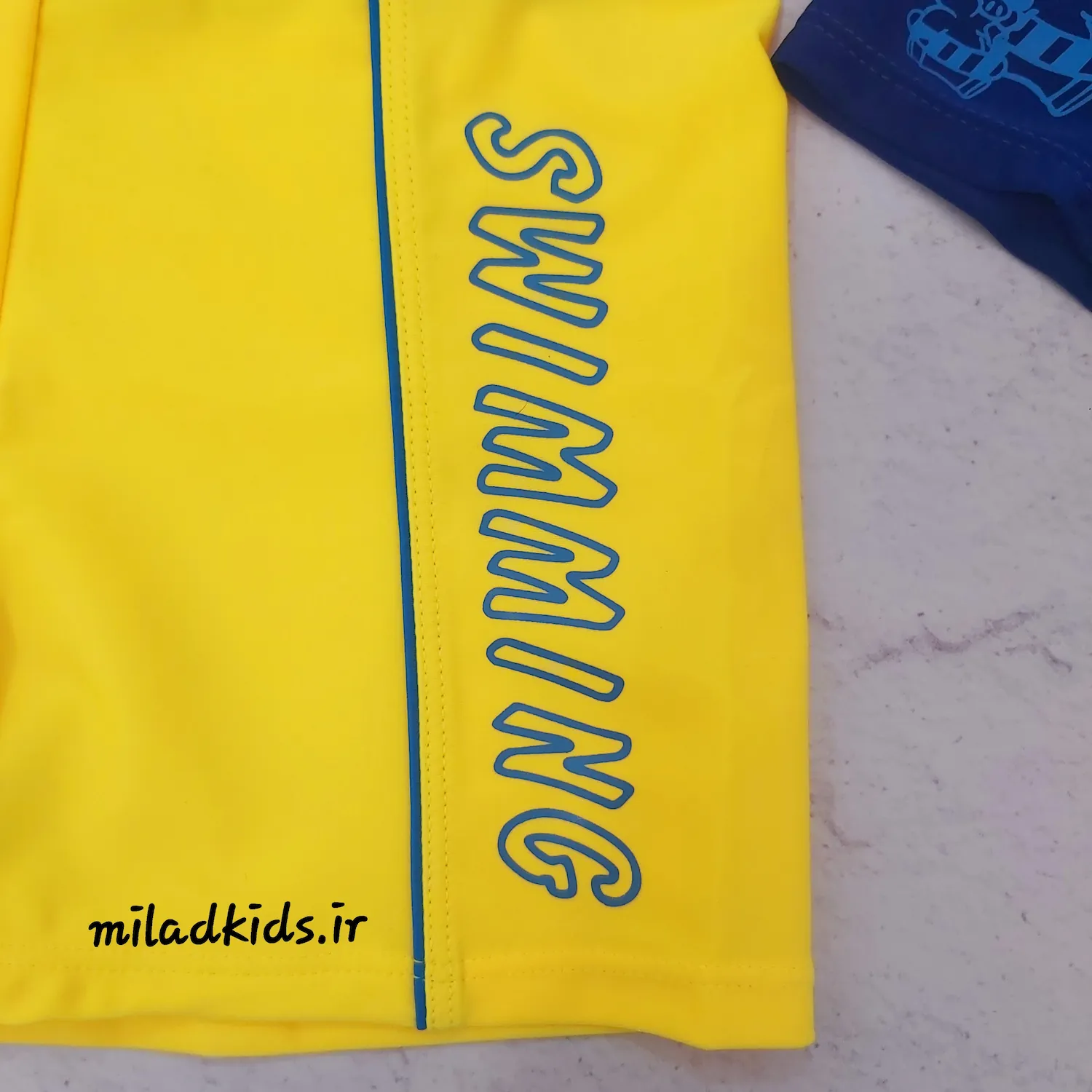 نوشته SWIMMING سمت چپ شرت شنای پسرانه از نمای نزدیک رنگ زرد